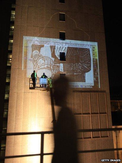 Three graffiti artists on a crane spray paint a wall of a high rise building in Bristol.