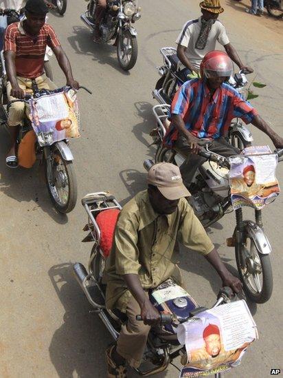 Men ride motorcycles bearing posters of Chukwuemeka Ojukwu