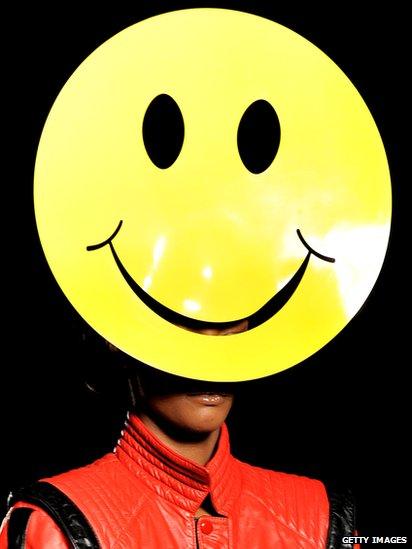 Model wearing a yellow smiley face hat.