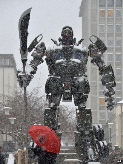 A passerby with an umbrella walks next to the sculpture Transformer by Chinese artist Bi Heng in snow in Kassel, central Germany, 12 March