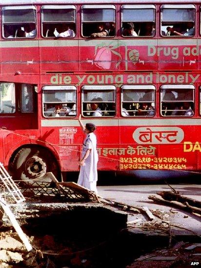 In this photograph taken on March 16, 1993, an Indian pedestrian is passed by a double-decker bus as she walks past bomb blast debris in Mumbai