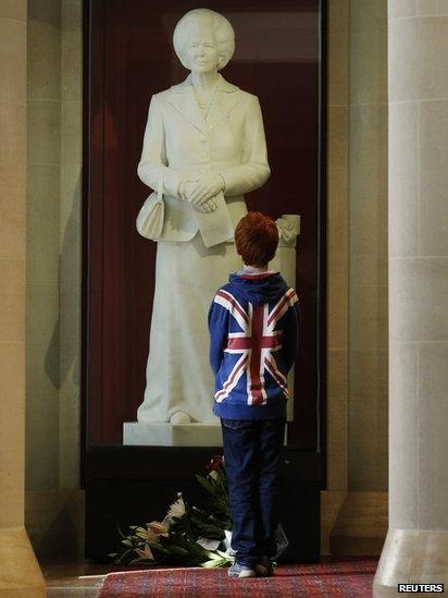 A boy stands in front of a statue of former British prime minister Margaret Thatcher, on display in the Guildhall Art Gallery in the city of London. Date: 8 April 2013. In 2002 a man decapitated the statute on display but it was later restored