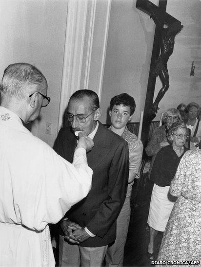 Former Argentine military leader Gen Jorge Rafael Videla takes communion from a priest of a local church, Buenos Aires, 30 December 1990. a day after he was released from prison