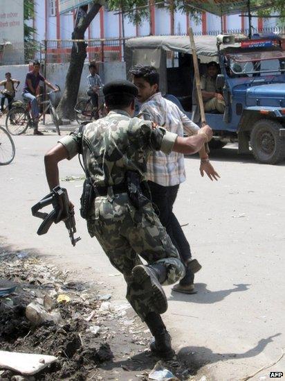 Policeman chases young male youth participating in street protests over school children deaths in Saran district of Bihar state on 17 July