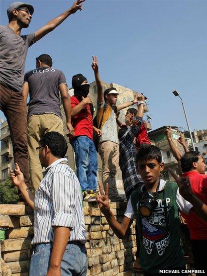 Protesters standing on a wall wave their arms in defiance