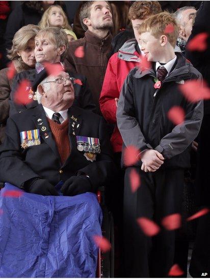 World War II veteran from Liverpool, England, Alan Rowe, left, looks up at a young boy as paper poppies fall during an Armistice Day ceremony under the Menin Gate in Ypres, Belgium