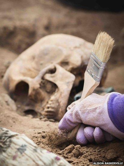 The team use paintbrushes to dust carefully around the bones as there may loose teeth and smaller bones that have fallen away in the grave