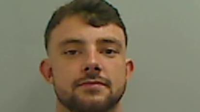 Mugshot of a young man with short dark hair and a close cropped beard.