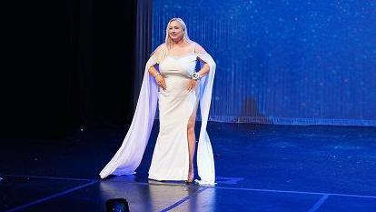 A woman wearing a white wedding dress stands on stage