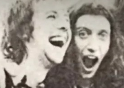 A black and white image of two men with long hair laughing with their mouths open