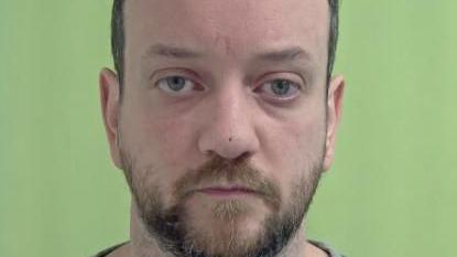 Police mugshot of Scott Goulden, who has short dark hair and a short beard. The background is green.