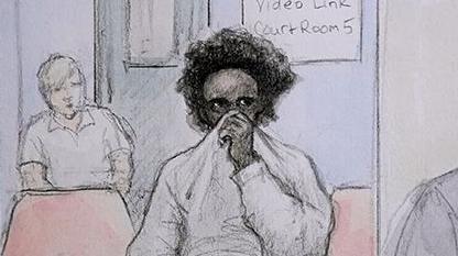 Court sketch of Axel Rudakubana at Liverpool Crown Court via videolink from HMP Belmarsh with curly dark hair holding his jumper up over his mouth and nose and a prison officer in the background