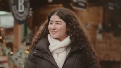 A woman with long curly dark hair walking through a Christmas market