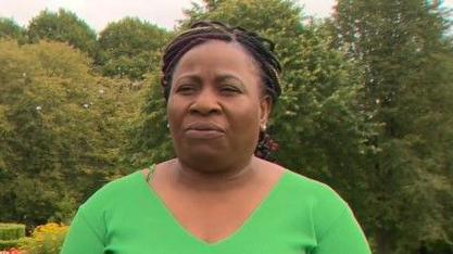 Beverly, a black woman, is standing outside in a green top