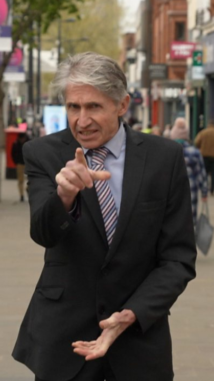 A man wearing a suit with grey hair stands on the streets of Swindon Town Centre