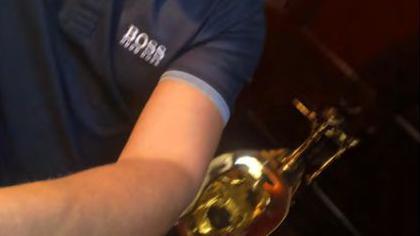 It shows a blurry image of a man's torso and arm. He's wearing a blue T-shirt. Just behind his arm is a solid gold toilet in the background.