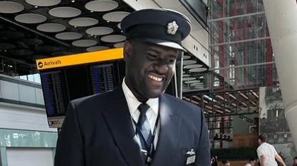 Yeboah in his British Airways uniform which includes a navy suit and hat. He is smiling and looking off-camera.