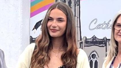 Alicia Woolley has a white cardigan and long brown curly hair in ringlet