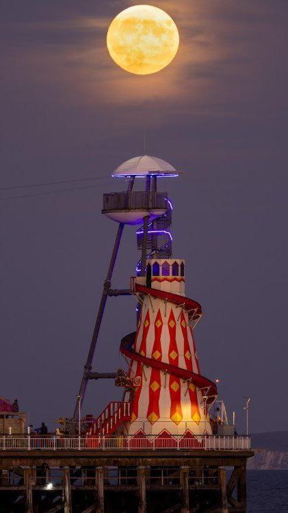 Pier with red white and yellow helter skelter ride on its tip with the bright moon above