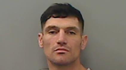 Mugshot of Aaron Thistlethwaite. He has a slight beard shadow and short dark hair. He may be attempting to look smouldering or aloof, but actually looks quite vacant.