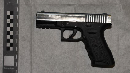 A black pistol with a silver barrel. It has been laid out on a white sheet.