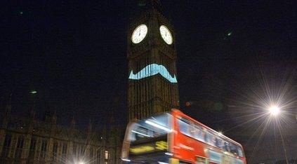 Big Ben with moustache projected on to it.