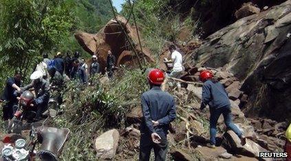 Rescuers try to remove rocks blocking a road