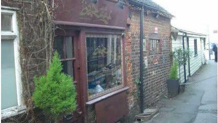 A brick building on the side of a path with a red shop front houses a Turkish restaurant. 