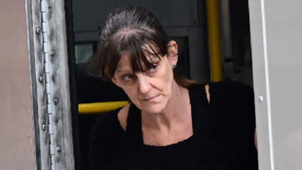 A woman with dark hair walking out of a police van. She had a black jumper dress on