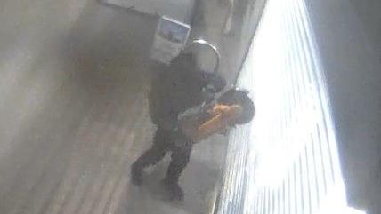 A man holding what appears to be an angle grinder outside a shop on CCTV footage