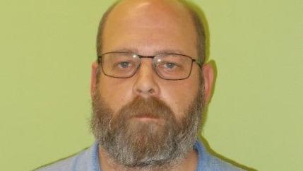 A mugshot of Benjamin Solowan. He is bald, is wearing glasses, and has a medium length brown and grey beard. He is staring into the camera blankly.