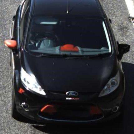 A CCTV still image from above, of a red and black Ford Fiesta on a road.