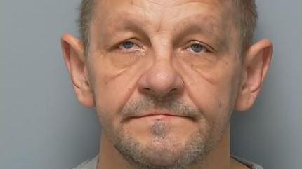 Damian Mazurkiewicz, an unshaven man with short, greying hair, looks straight at the camera in a police custody image