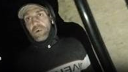 A blurry image of a man in a black hoodie. He seems to have a cap and light stubble.