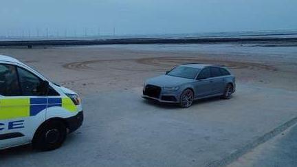 Police van facing a car with circles scored into the sand