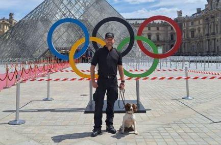 A police officer in all black clothes holds the lead of a brown and whit