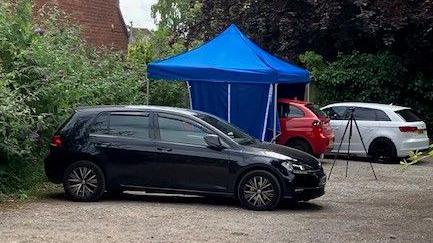 A red car covered by a blue tent next to two cars