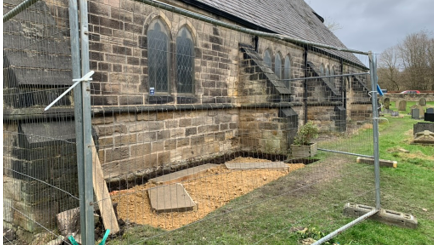 A wall of the church with railings around an area which has two slabs ready for a memorial to be installed 