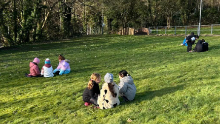 Children in groups in their coats sitting on the grass.