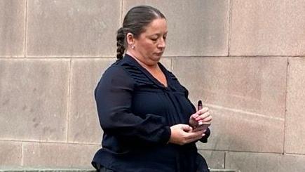 A woman in a navy blouse with a mobile phone in one hand and a vape in the other.