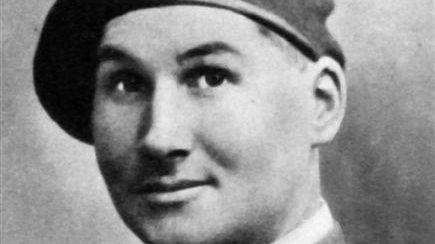 A black and white photo of a male soldier. He is wearing a tie with badges on the collar of his shirt. He is also wearing a hat with a parachute regiment badge on.