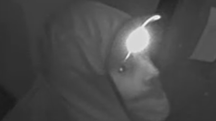 A blurry police handout of someone wearing a hood and what appears to be a mask over their mouth and a headtorch.