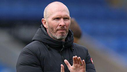 Shrewsbury Town head coach Michael Appleton is wearing his black puffer coat and clapping the crowd after a game
