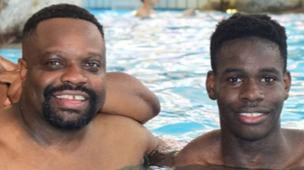 Two men stand side by side in a swimming pool, they are both smiling at the camera.
