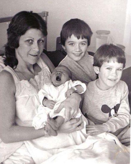 A woman in a hospital bed holdin a baby with two other young boys at the bedside.