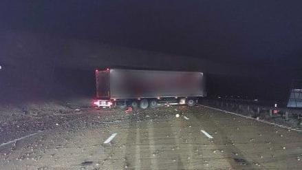 A lorry trailer parked across four lanes of traffic at night. There is debris scattered across the road