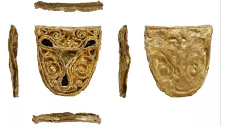 The photo shows four long pieces of metal, and one crest-shaped gold item in the middle which has intricately weaved patterns on it. The crest is repeated from the back next to it