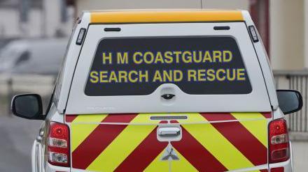 The back of a HM Coastguard search and rescue vehicle. It is a white 4x4 and has yellow and red emergency markings on.