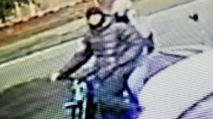 A screenshot of CCTV footage showing two people riding a  electric bike, wearing clothing which conceals their faces.
