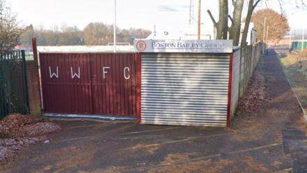 The entrance to Walsall Wood football club. It is autumn and there are leaves on the ground. There is a fence with WWFC lettering.